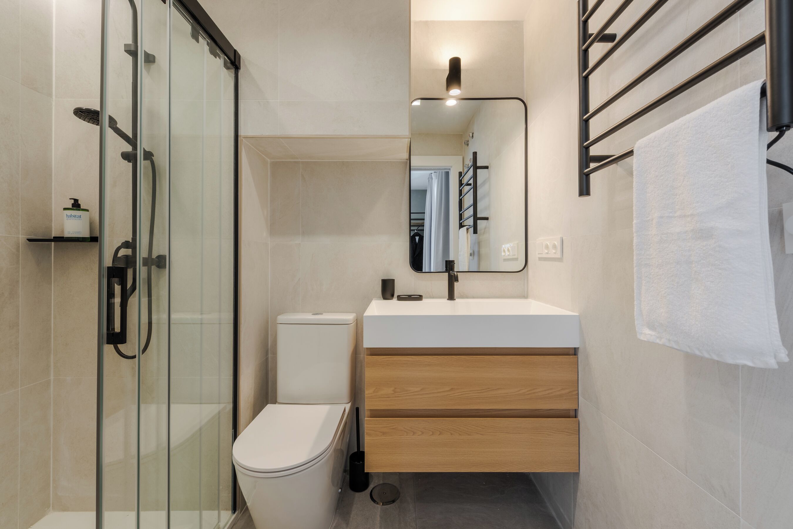 A modern bathroom with a glass shower enclosure, a white toilet, a wooden vanity with a mirror, and a towel rack.