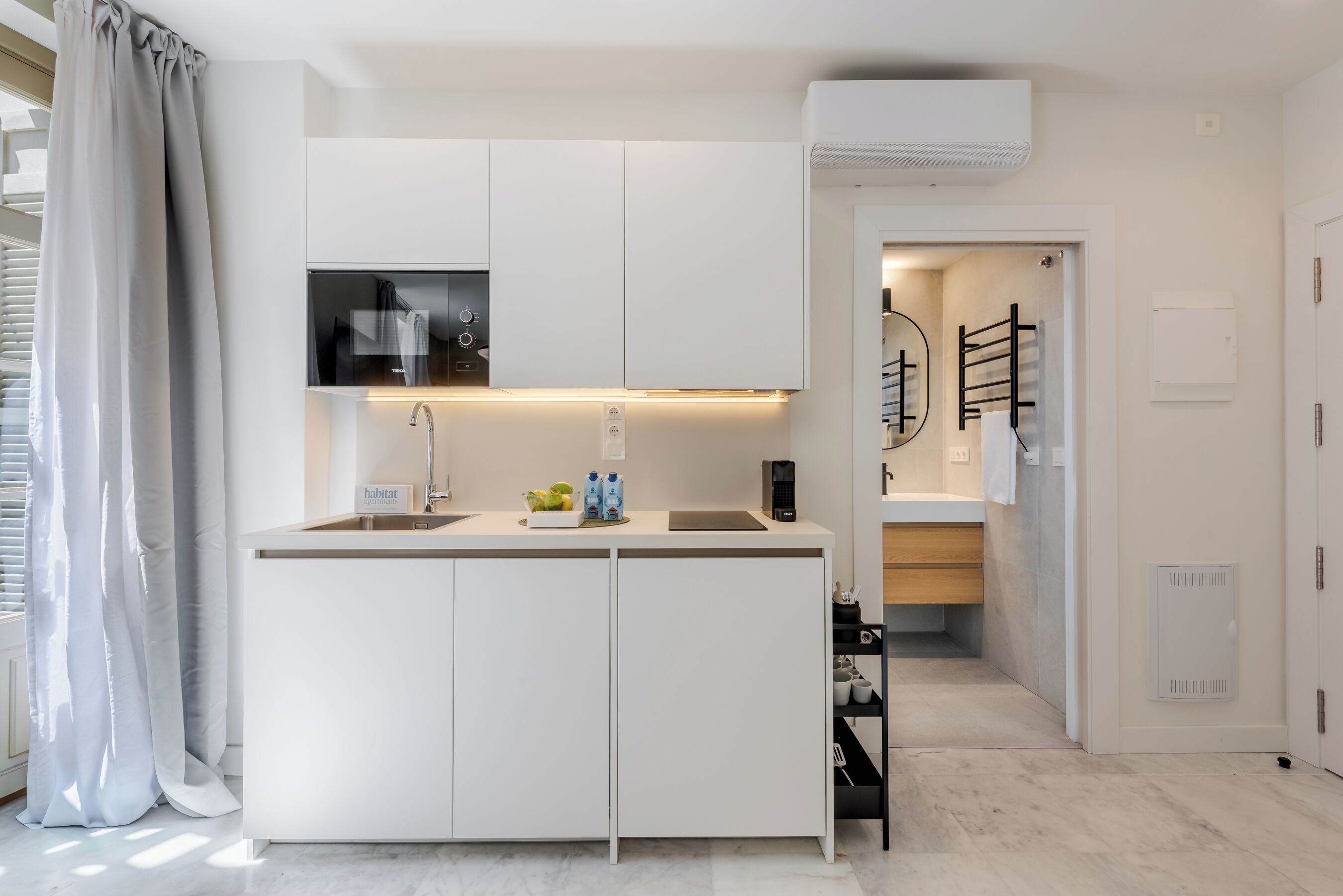Cocina moderna con gabinetes blancos, horno empotrado y televisor de pantalla plana sobre la encimera.