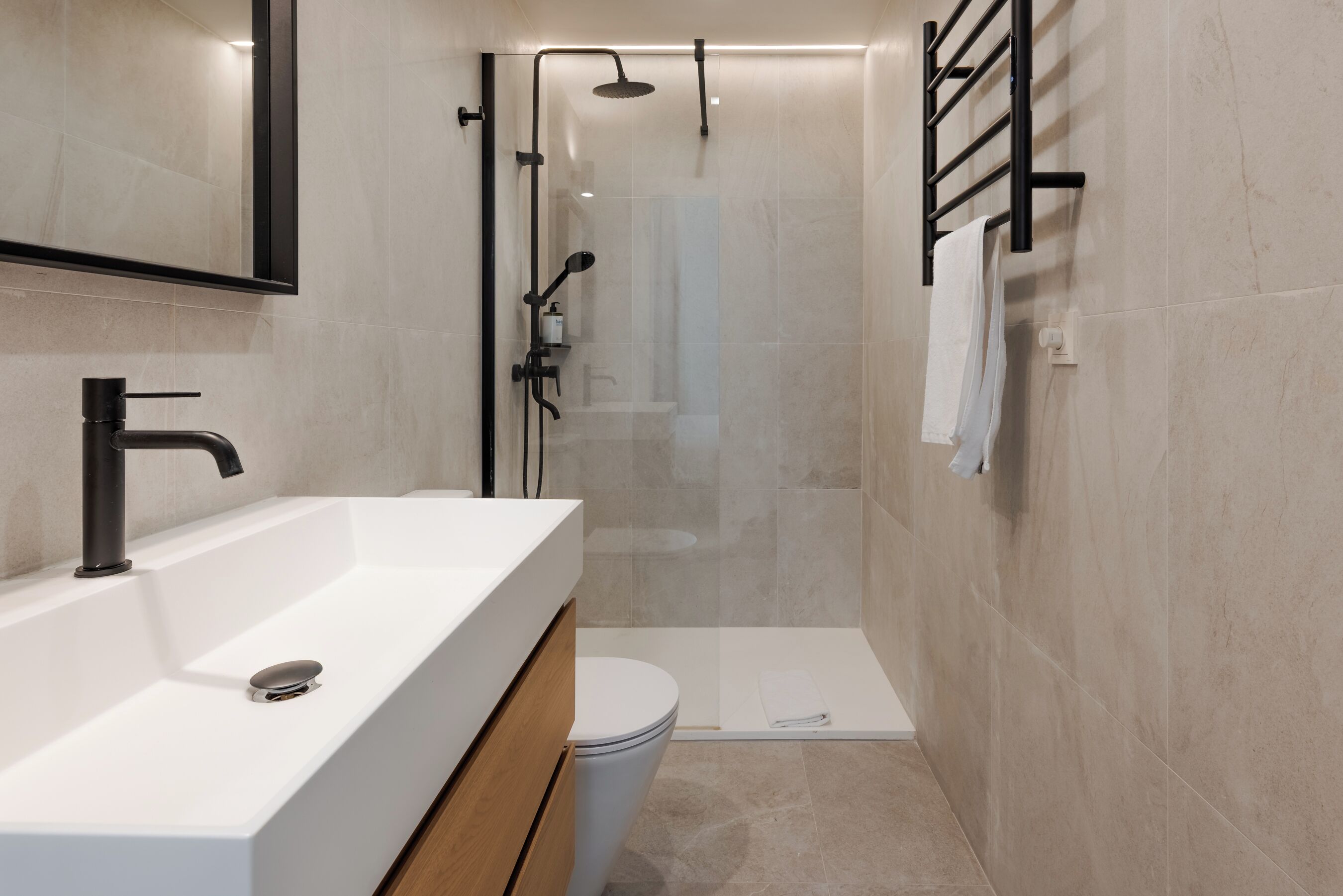 A modern bathroom with a white sink, a mirror, a shower enclosure, and a toilet.
