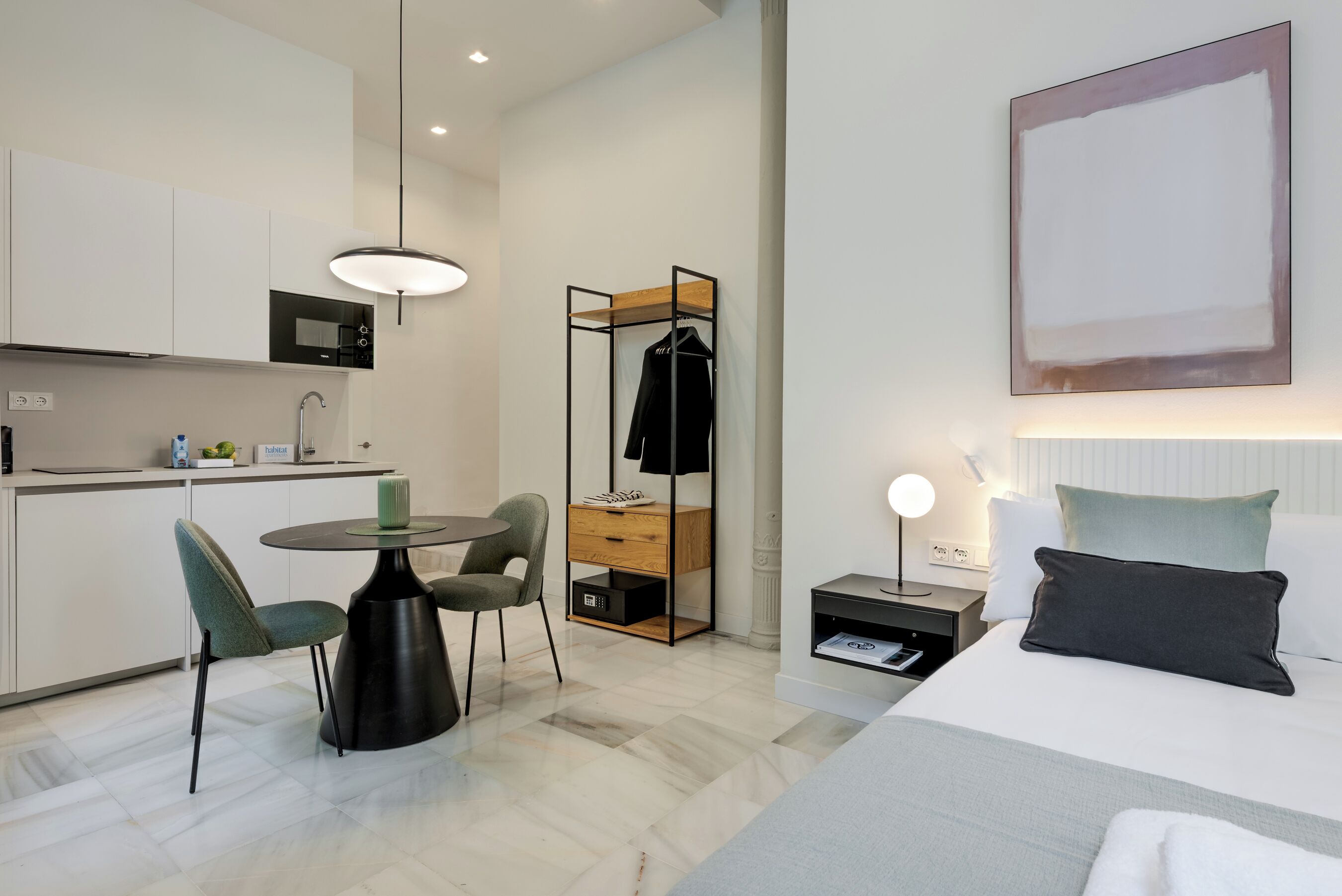 Ett modernt hotellrum med en säng, ett sängbord, en lampa och en matplats med ett bord och stolar.