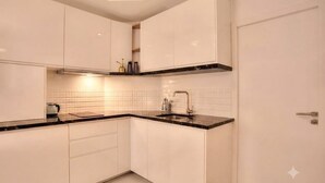A modern kitchen with white cabinetry, a black countertop, and a tiled backsplash. - Celine 29 (Paris)