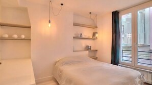 A bedroom with a bed, built-in shelves, and a window with curtains. - Celine 29 (Paris)