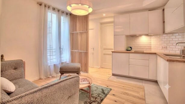 A compact living space with a kitchenette, a sofa, a small table, and a window with curtains. - Celine 29 (Paris)