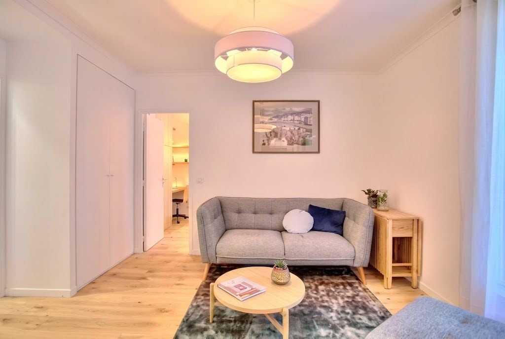 A modern living room with a grey sofa, a round coffee table, and a pendant light.