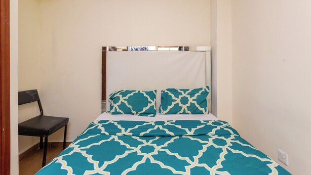 A small, single-bed room with a canopy bed, a chair, and a bedside table. - Skyline View Palace Apartment (Nairobi)