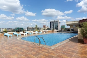 Una piscina en la azotea con sillones de descanso y vistas a la ciudad.