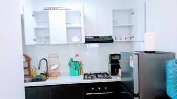 A compact kitchen with white cabinets, a gas stove, a black refrigerator, and a small sink.