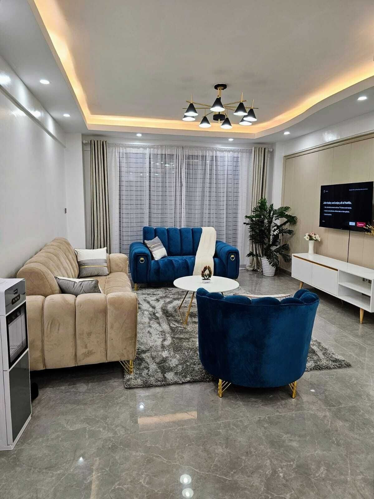 A modern living room with a sofa, armchair, and coffee table, a flat-screen TV, and a potted plant.