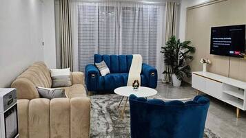 A modern living room with a sofa, armchair, and coffee table, a flat-screen TV, and a potted plant.
