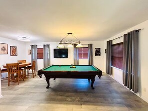 A pool table in a room with a dining table and chairs, a flat-screen TV, and a ceiling light fixture. - Your Tampa Bay Vacation Entertainment Home (Tampa)