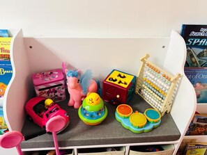 Eine Aufbewahrungsbox mit Spielzeug und Büchern, darunter ein rosafarbenes Spielzeugauto und eine Puppe mit blauen Haaren.