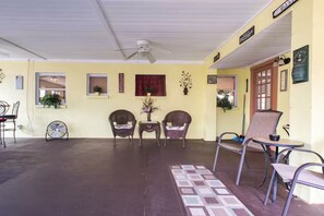 Un espace extérieur abrité, doté de chaises, d’un ventilateur et d’un sol à carreaux.