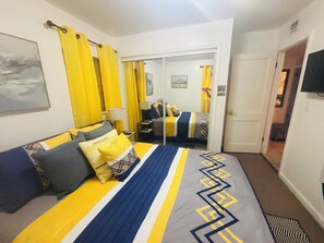 Une chambre d’hôtel avec un lit, une table de chevet, une lampe, une porte et un téléviseur.