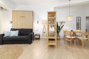 A modern living room with a sofa, a wooden wardrobe, a dining area with a table and chairs, and a hanging light fixture. - Travel Habitat Loft Parque de Cabecera 2 (Valencia)