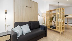 A modern living room with a dark sofa, a wooden bookshelf, and a lamp. - Travel Habitat Loft Parque de Cabecera 2 (Valencia)