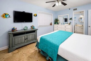 Une chambre à coucher comprenant un lit, une commode, un téléviseur et un ventilateur de plafond.
