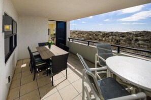 Ein Balkon mit Tisch und Stühlen, Blick auf den Strand und eine Tür zu einem Innenraum.