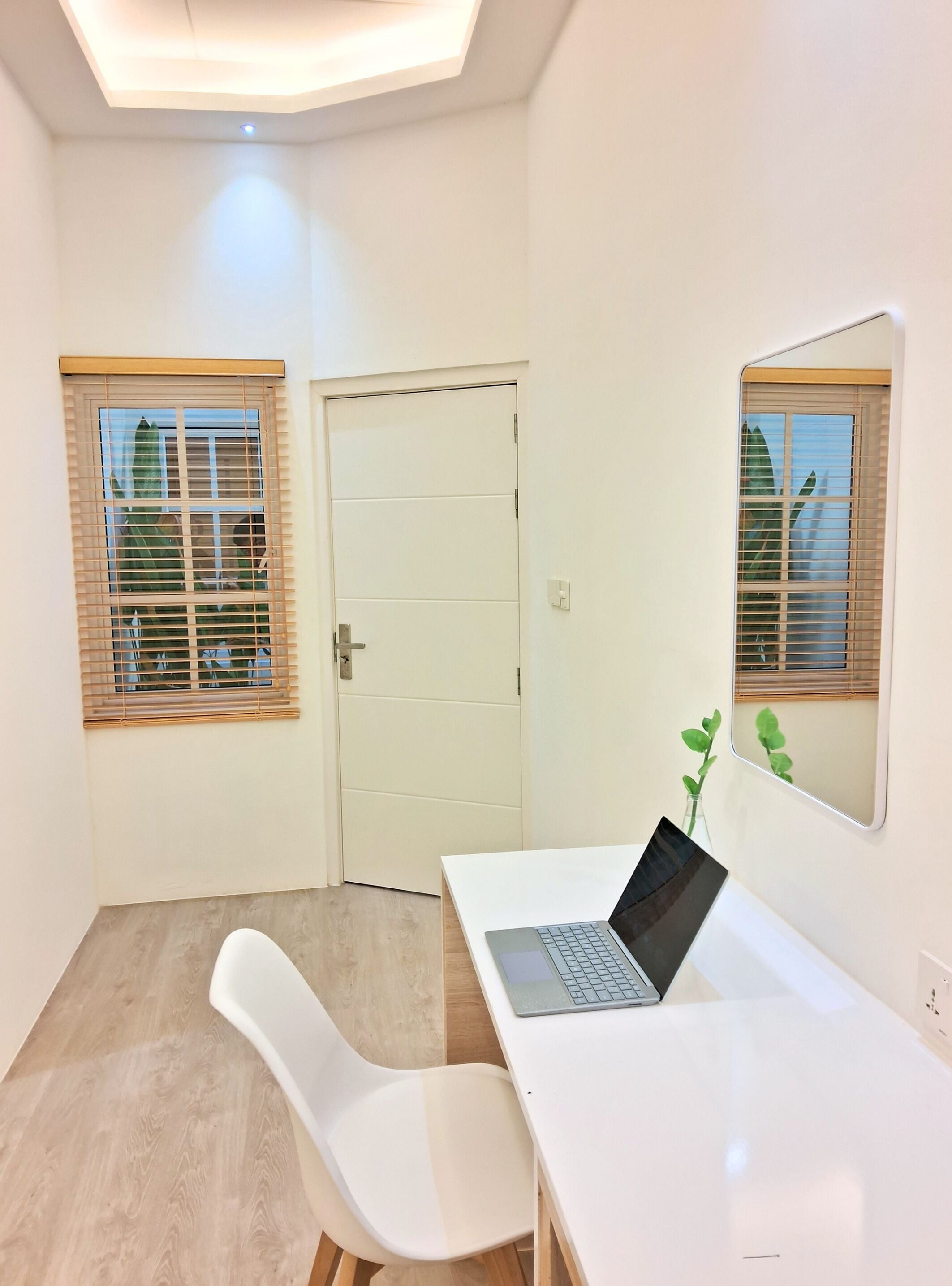 A room with a white desk, a laptop, a white chair, and a door with a window.