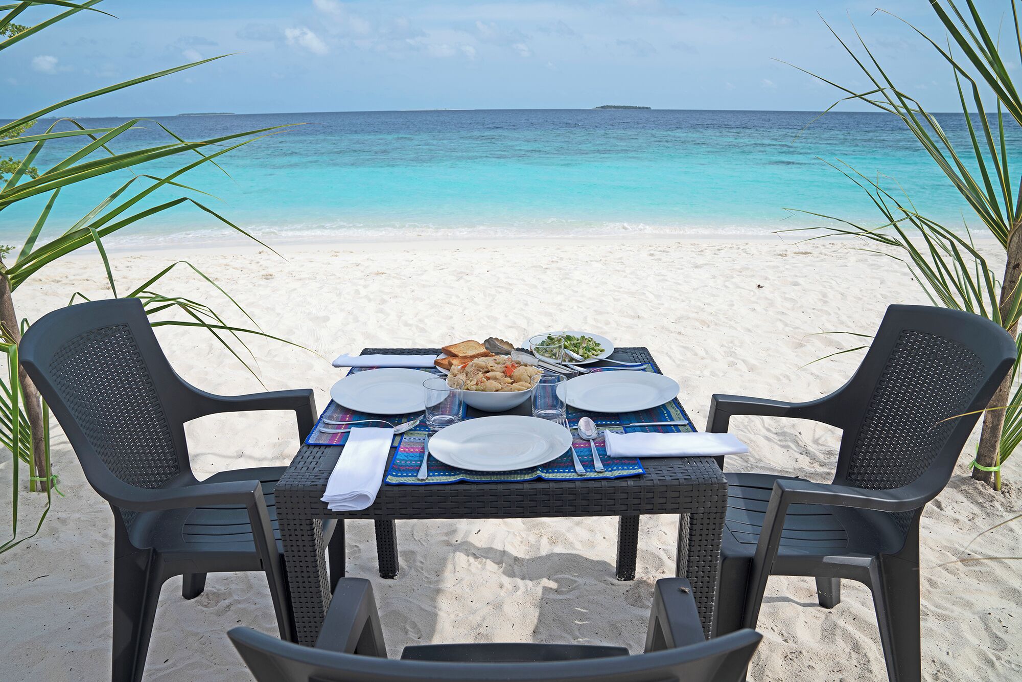 Una mesa puesta en la playa con dos sillas, un plato de comida y vista al océano.