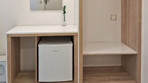 Quarto compacto com escrivaninha branca, espelho, uma pequena planta e um closet espaçoso com portas de madeira.