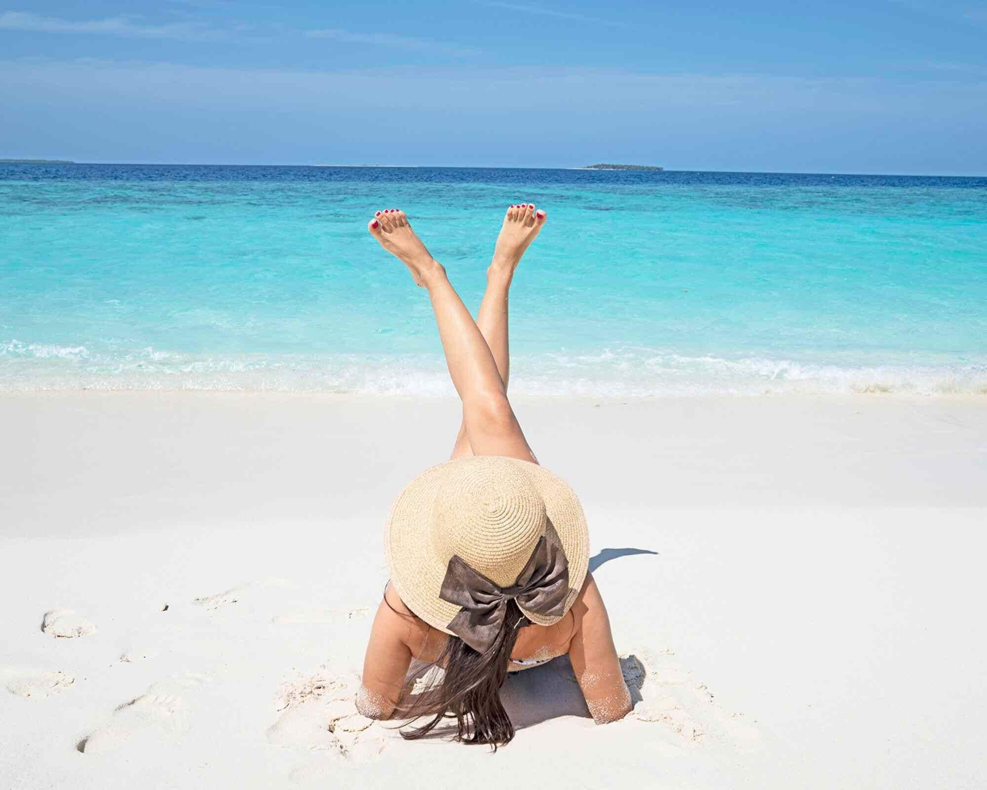 Una persona acostada en la playa con las piernas levantadas, mirando al océano.