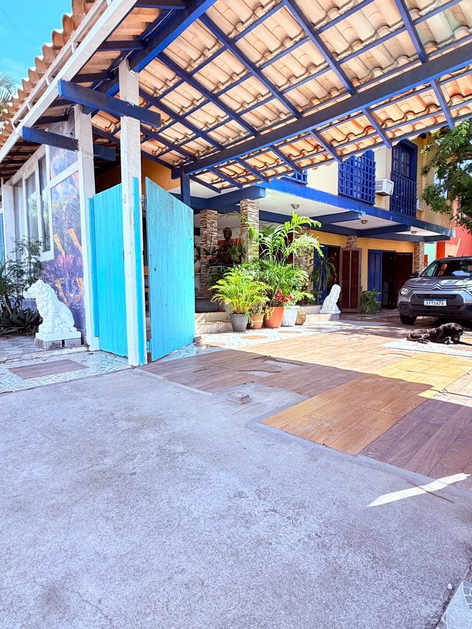 A covered outdoor area with a car parked, potted plants, and a statue.