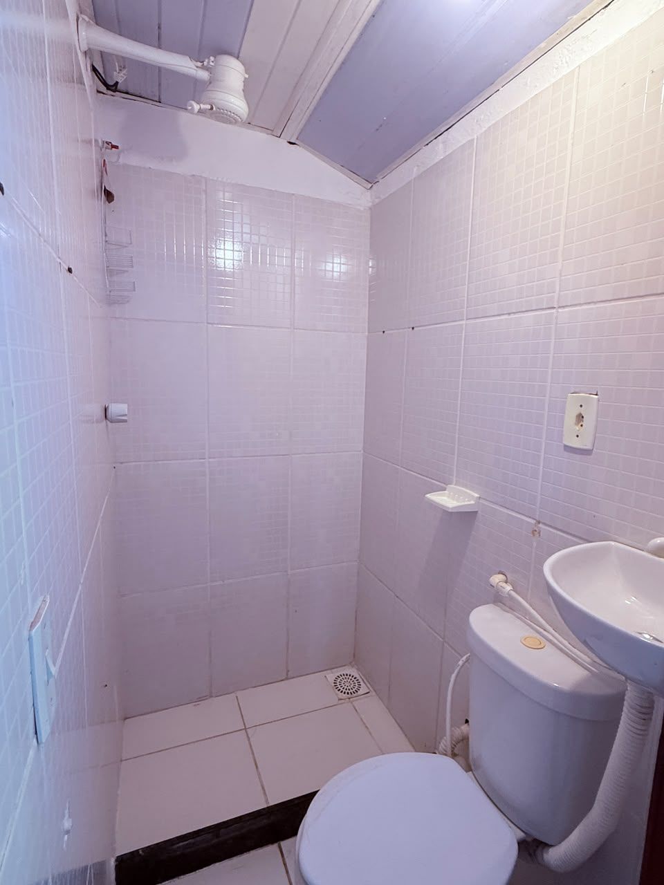 A bathroom with white tiles, a toilet, a sink, and a shower area.
