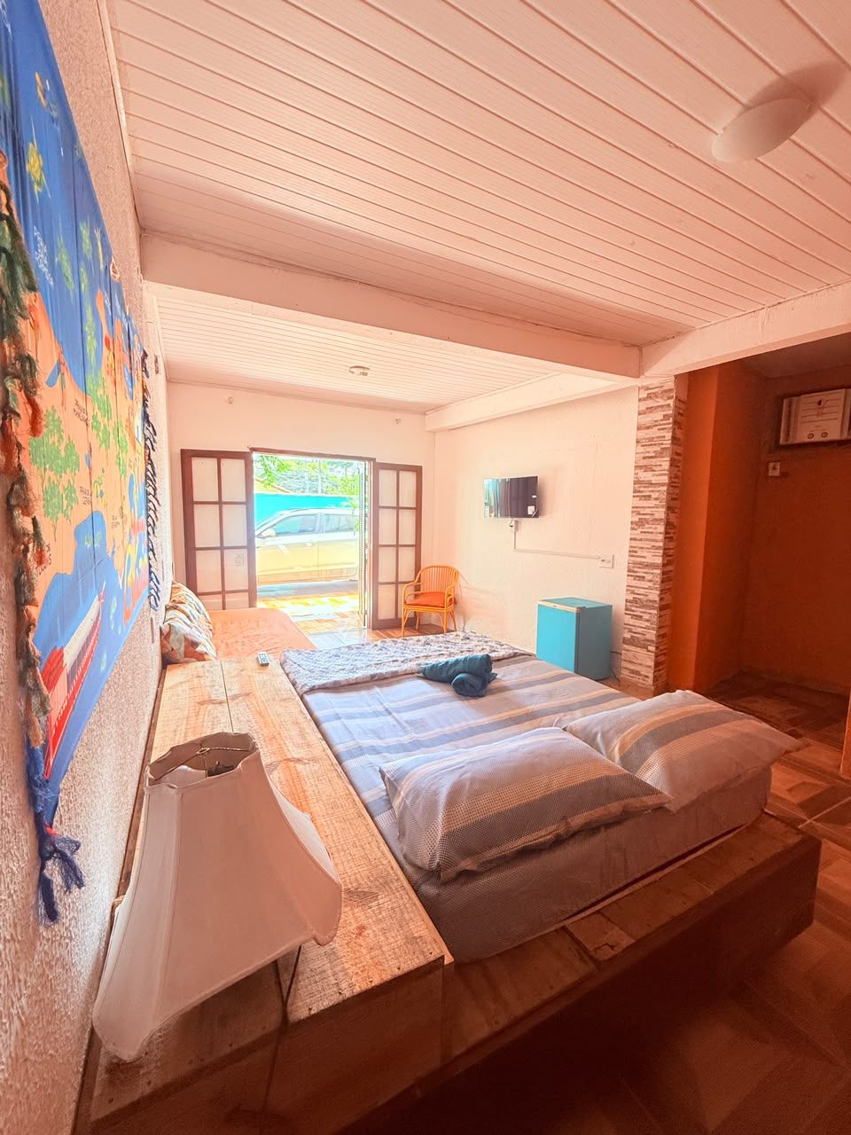 A room with a bed, a TV, a chair, and a large window.