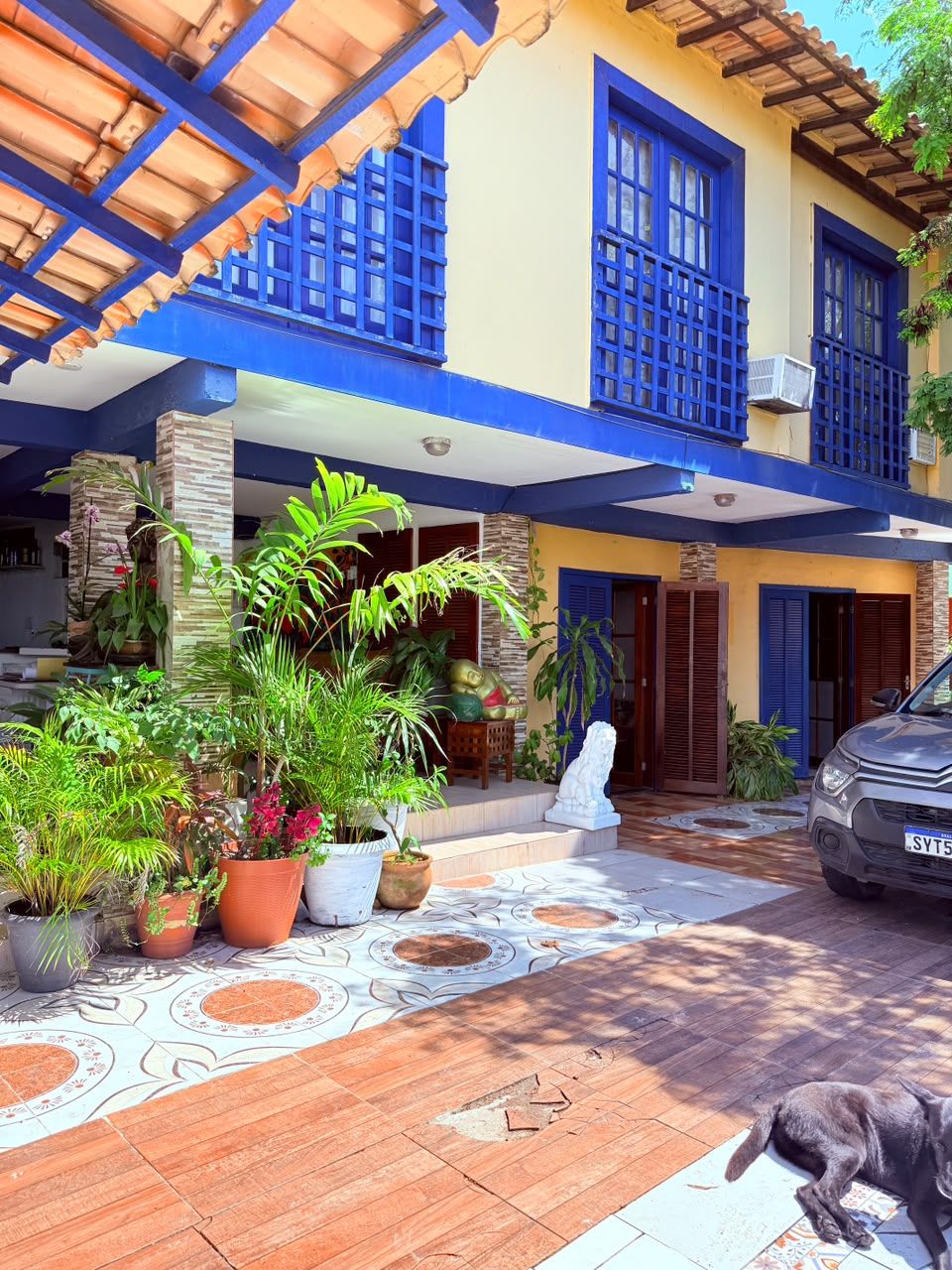 A two-story building with blue-framed windows and a covered entrance. There are potted plants and a statue in the foreground.