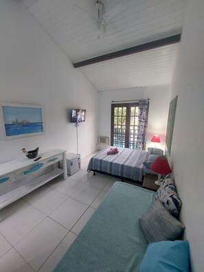 A room with a bed, a television, a desk, and a window with curtains. - Pousada E Apartamento Buda Buzios (Buzios)