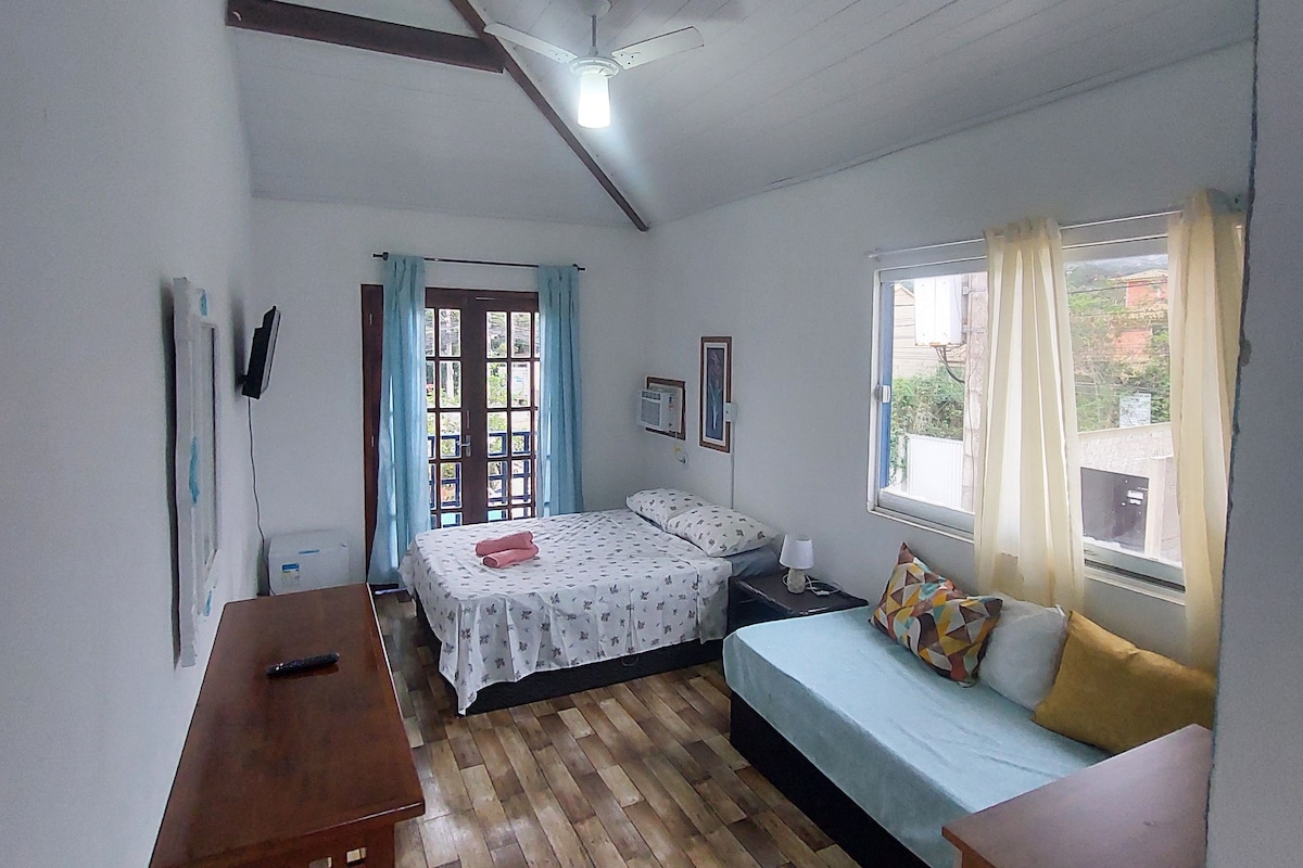 A room with a bed, a sofa, a wooden table, and a ceiling fan.