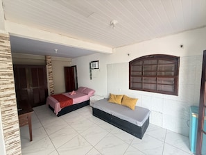 A room with two beds, a small table, and a window with a decorative frame. - Pousada E Apartamento Buda Buzios (Buzios)