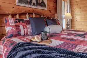 Ein gemütliches Schlafzimmer mit einem hölzernen Kopfteil, einer gesteppten Bettdecke, einem Nachttisch mit Lampe und einem Tablett mit Gebäck.
