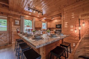 A wooden cabin interior with a kitchen island, bar stools, and a dining table set. - Rocky Top Retreat | Accessible | Mt Views |Hot Tub (Sevierville)