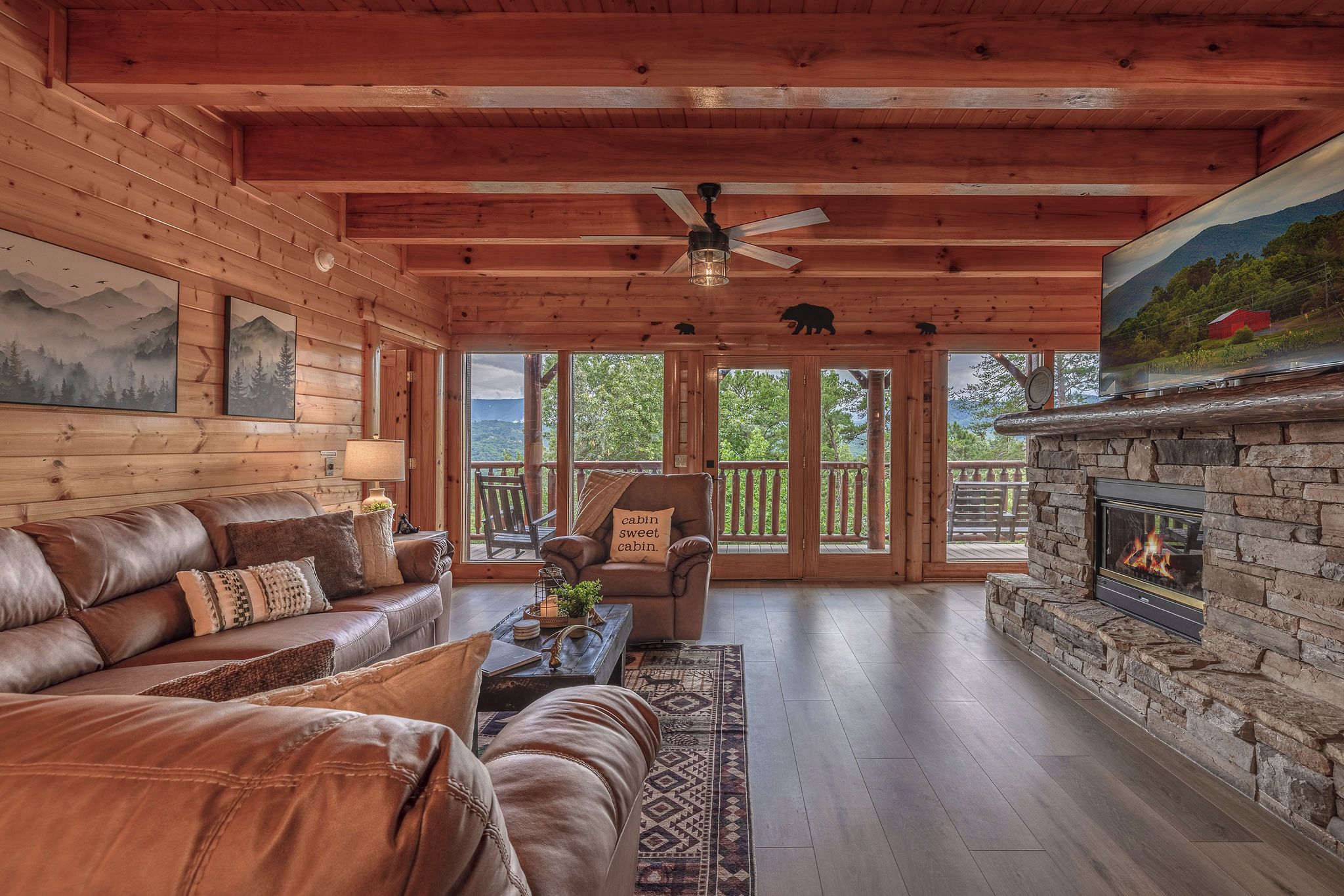 A cabin interior with a leather sofa, a stone fireplace, and a view of the outdoors.