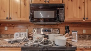 Una cucina con mobili in legno, un forno a microonde, un fornello e diversi utensili da cucina.