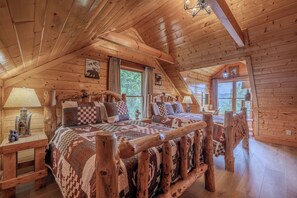A log cabin bedroom with a large bed, wooden headboard, and a view of the outdoors. - Rocky Top Retreat | Accessible | Mt Views |Hot Tub (Sevierville)