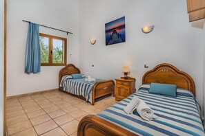 Ein Hotelzimmer mit zwei Betten, einem fensterbelaubten Fenster, einem Wandbild und einem Nachttisch mit einer Lampe.