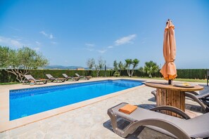 Ein Swimmingpool mit Liegestühlen und Sonnenschirm, umgeben von viel Grün und blauem Himmel.
