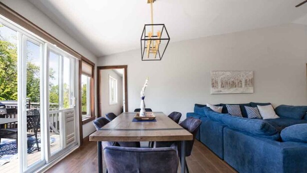 A spacious room with a dining table, chairs, a blue sofa, and a pendant light. - Rama Ridge with Basketball Court, Hot Tub, Sauna (Orillia)