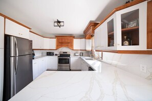 Eine Küche mit weißen Schränken, einem Edelstahl-Kühlschrank, einem eingebauten Backofen und einer Marmorarbeitsplatte.