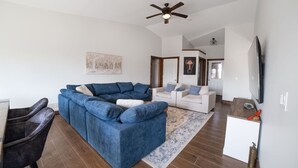 A living room with a blue sectional sofa, a white sofa, a TV, and a ceiling fan. - Rama Ridge with Basketball Court, Hot Tub, Sauna (Orillia)