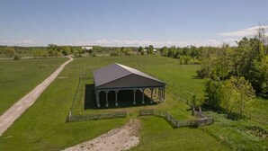 A large, open field with a single building featuring a covered porch and a fenced area. - Rama Ridge with Basketball Court, Hot Tub, Sauna (Orillia)