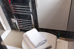 Une salle de bain comprenant des toilettes, une serviette, un porte-serviettes et un espace douche.