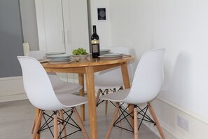 Una mesa de comedor con cuatro sillas blancas, una botella de vino y un bol de uvas verdes.