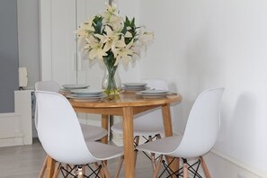 Ein Essbereich mit einem runden Holztisch, gedeckt für vier Personen, weißen Stühlen und einer Vase mit weißen Blumen.