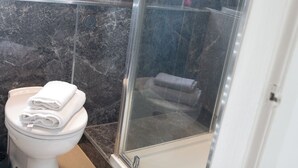 Une salle de bain avec des toilettes, une douche à parois de verre et un sol en marbre.