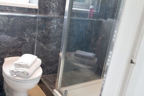Ein Badezimmer mit Toilette, einer gläsernen Duschkabine und einem Marmorboden.