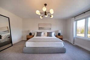 Ein Schlafzimmer mit einem großen Bett, Nachttischen, einer Chandelüster, einem Gemälde und einem Fenster mit Vorhängen.