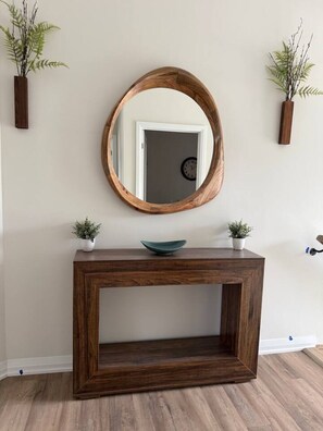 Um console de madeira com um espelho em cima, ladeado por duas plantas em vasos.